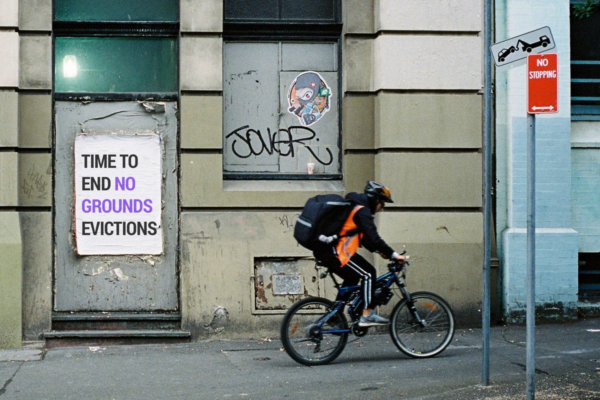 Person on a bike riding past a poster with the words 'time to end no grounds evictions'