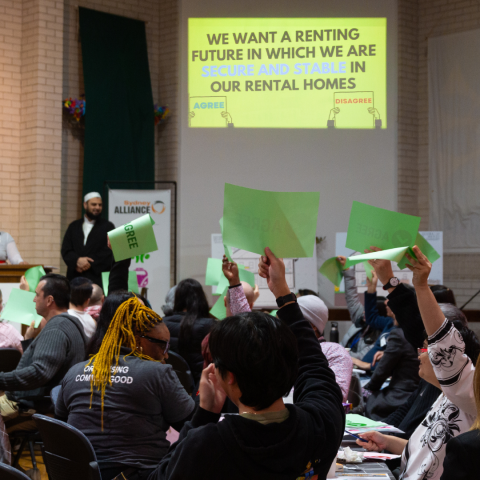 Renters seated voting with green paper and hands raised at Revesby Renters' Forum, indicating agreement with statement 'We want a renting future in which we are secure and stable in our rental homes.'